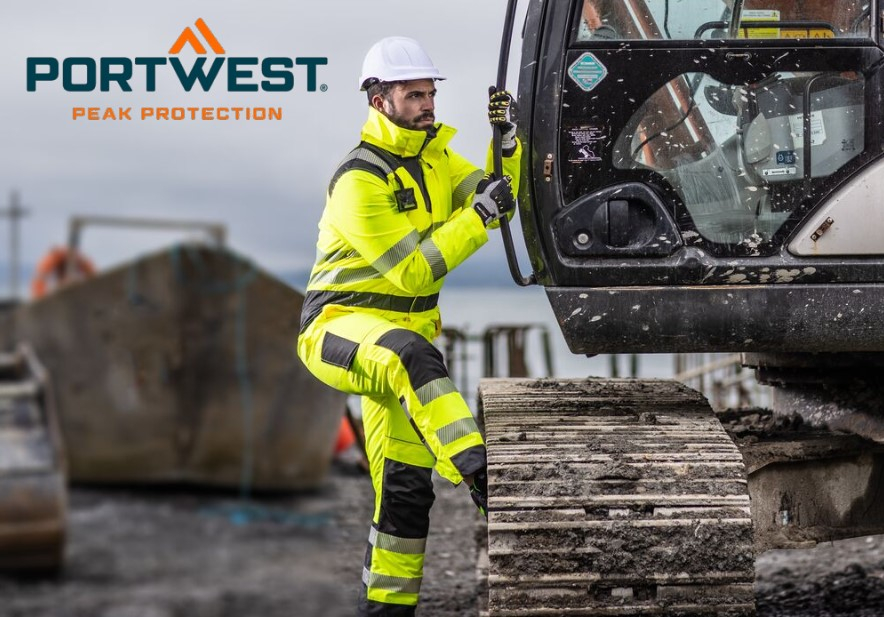 Een arbeider, gekleed in een felgeel veiligheidspak met reflecterende strepen, een witte helm en handschoenen, klimt in een bouwmachine. Op de achtergrond is een bouwplaatsomgeving te zien met bouwapparatuur en een grijze lucht. Linksboven op de foto staat het logo "Portwest" met de slogan "Peak Protection". Er wordt een link gegeven naar onze selectie van verschillende werkoveralls.