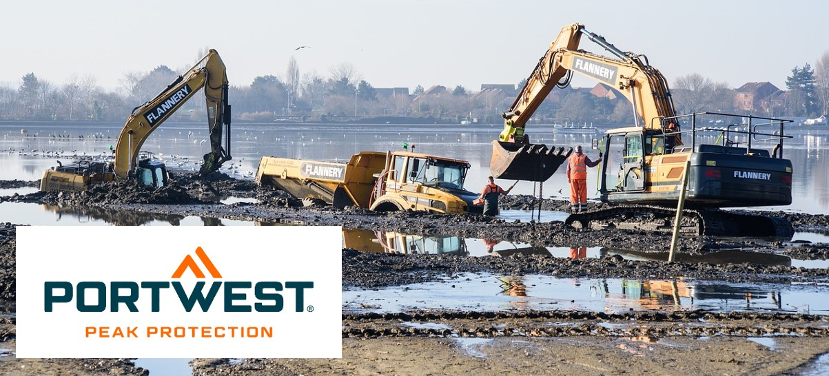 Bouwplaatsscène met graafmachines en grote machines. Er liggen plassen en modder op de grond, de lucht is blauw en aan de horizon zie je enkele huizen en bomen.